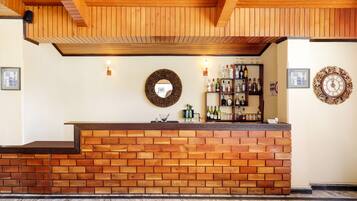 Un área de recepción con un mostrador de ladrillo, techo de madera, luces fijadas en la pared, un espejo, un reloj y un estante con botellas.