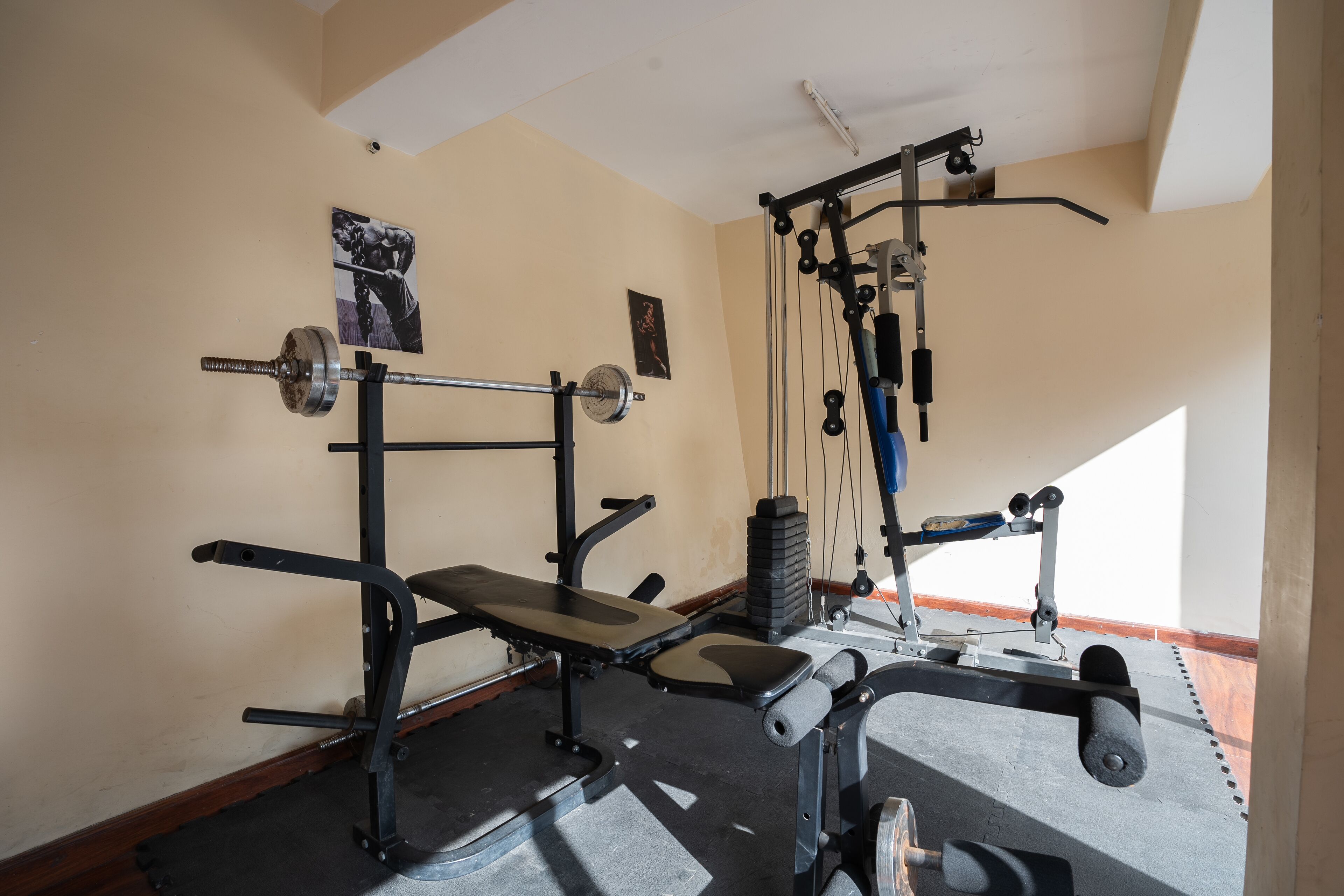 Une salle de sport équipée de matériel de musculation, d’un banc et d’un support mural pour les poids.