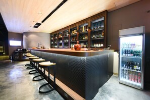 A bar area with a long counter, stools, shelves with bottles, and a refrigerator stocked with drinks. - Simple Life (Kaohsiung)