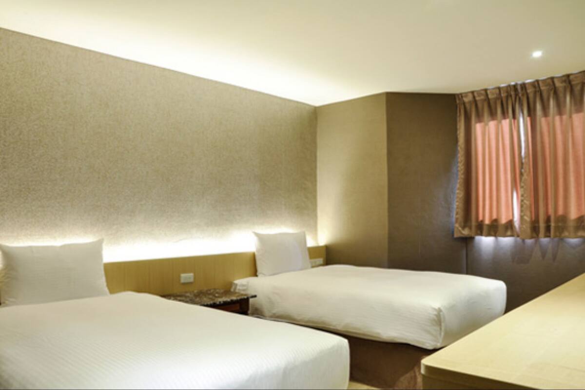 A hotel room with two beds, a desk, and a window with curtains.