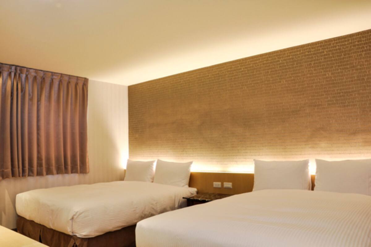 A hotel room with two beds, a brick accent wall, and a curtain on the left.