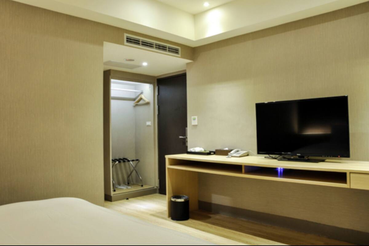 A hotel room with a bed, a TV on a wooden stand, a coat rack, and a door leading to a bathroom.