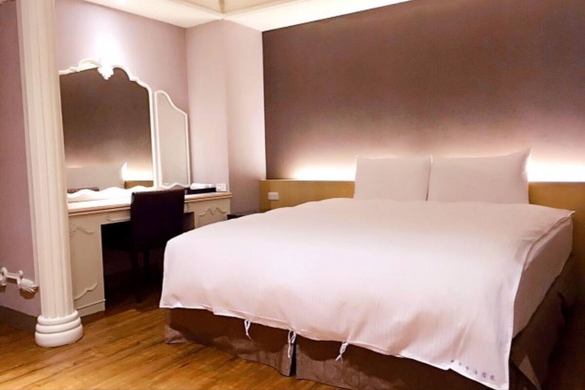 A bedroom with a large bed, a desk with a chair, and a mirror.