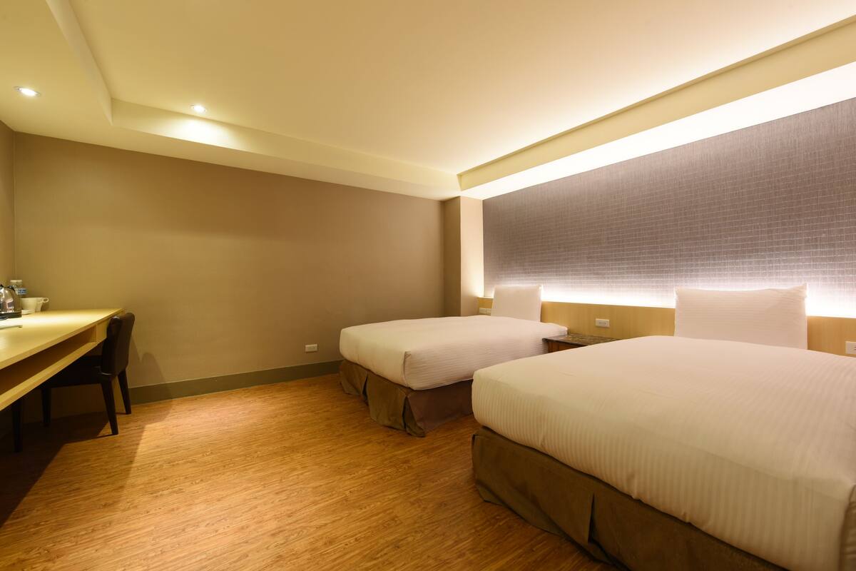 A hotel room with two beds, a desk, and a chair.