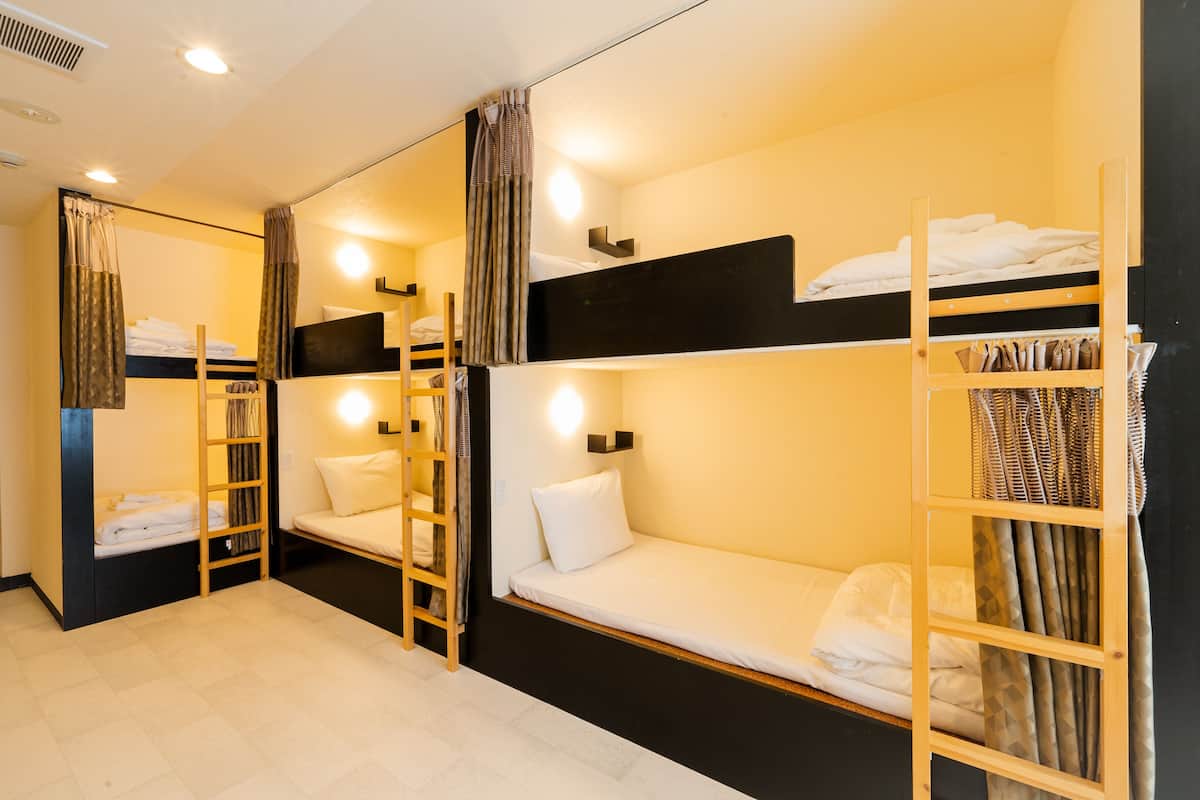 A dormitory room with bunk beds, a ladder, and a shelf with folded clothes.