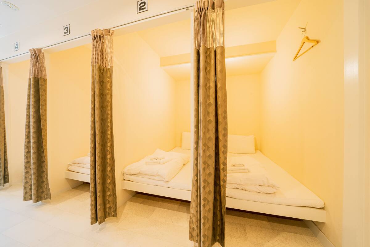 A row of single beds in a hotel room, each with a curtain and a hanging towel rack.