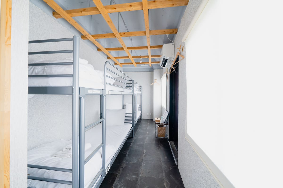 A narrow corridor with bunk beds on one side and a wall-mounted air conditioning unit on the other.