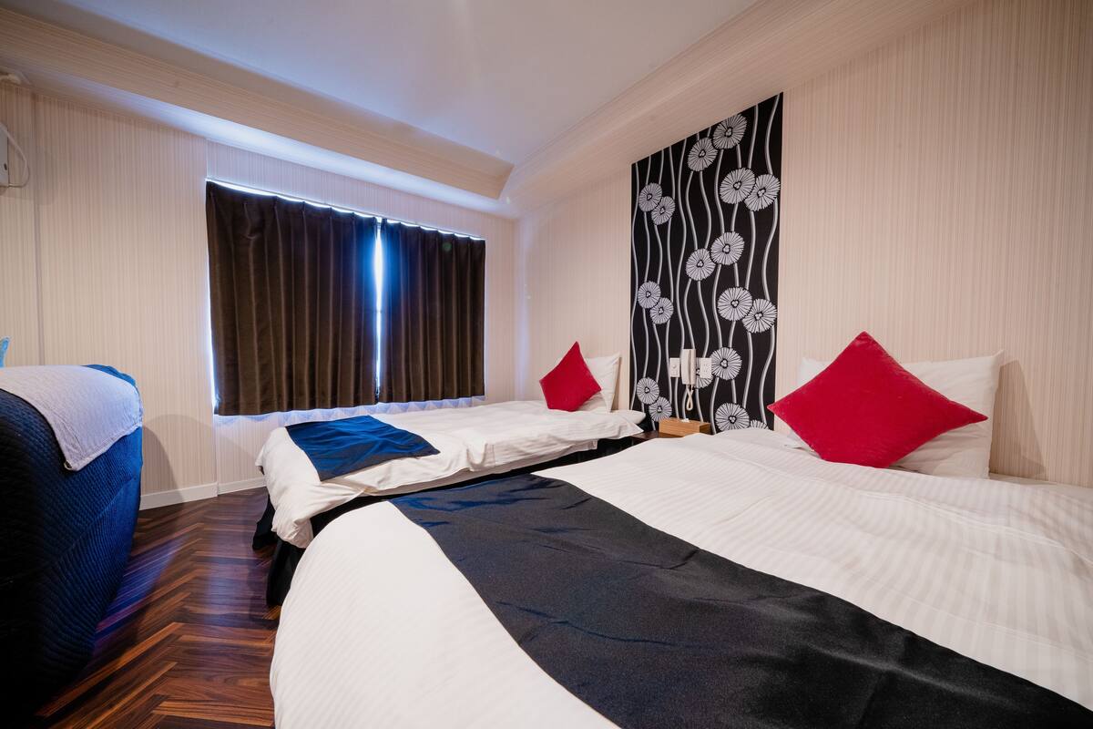 A hotel room with two beds, a window with curtains, a wall with a floral pattern, and a blue couch.