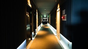 A long, narrow hotel corridor with doors on both sides, illuminated by overhead lights, leading to a brightly lit room at the end. - Hotel Pagoda (Nara)