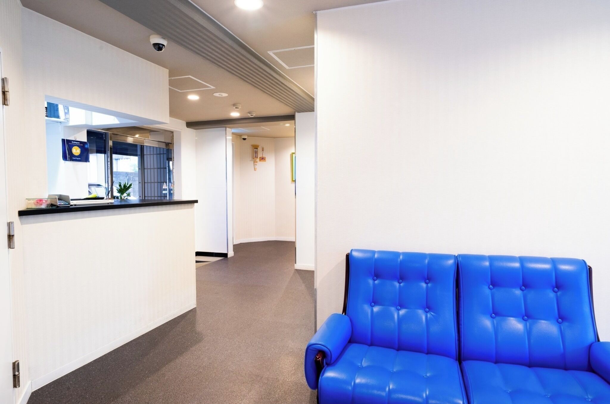 A modern hotel lobby with a reception desk, a blue leather sofa, and a hallway leading to other areas.