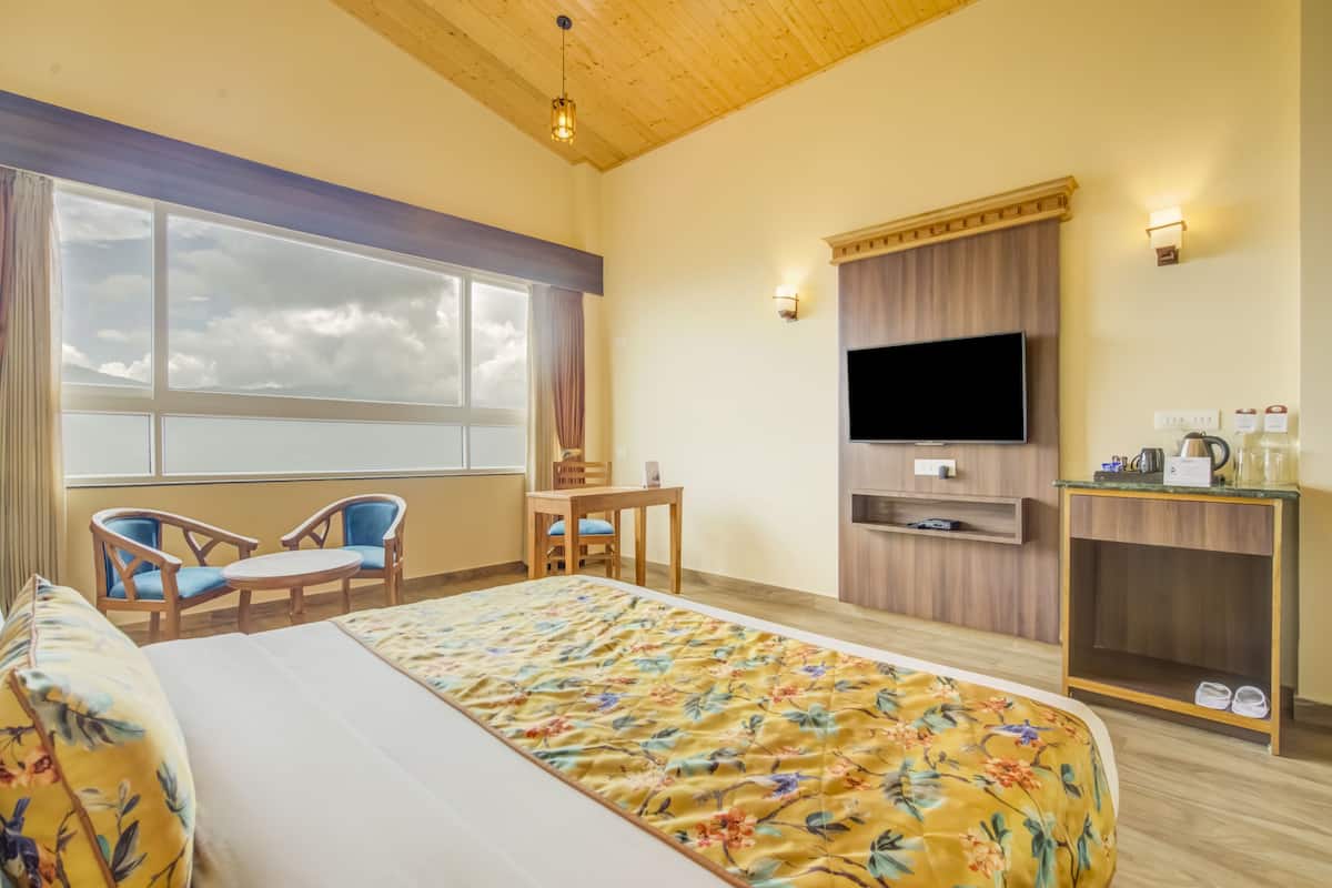 A hotel room with a bed, two chairs, a desk, a TV, and a small kitchenette.