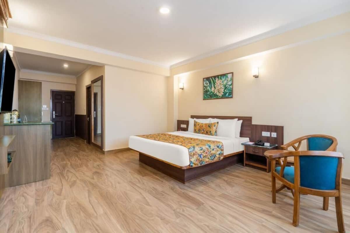 A hotel room with a bed, a desk, a chair, a painting on the wall, and a wooden floor.