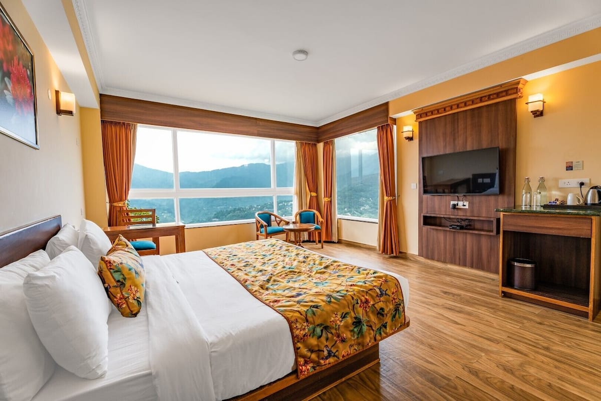 A hotel room with a large bed, a desk, a chair, a television, and a view of the mountains.
