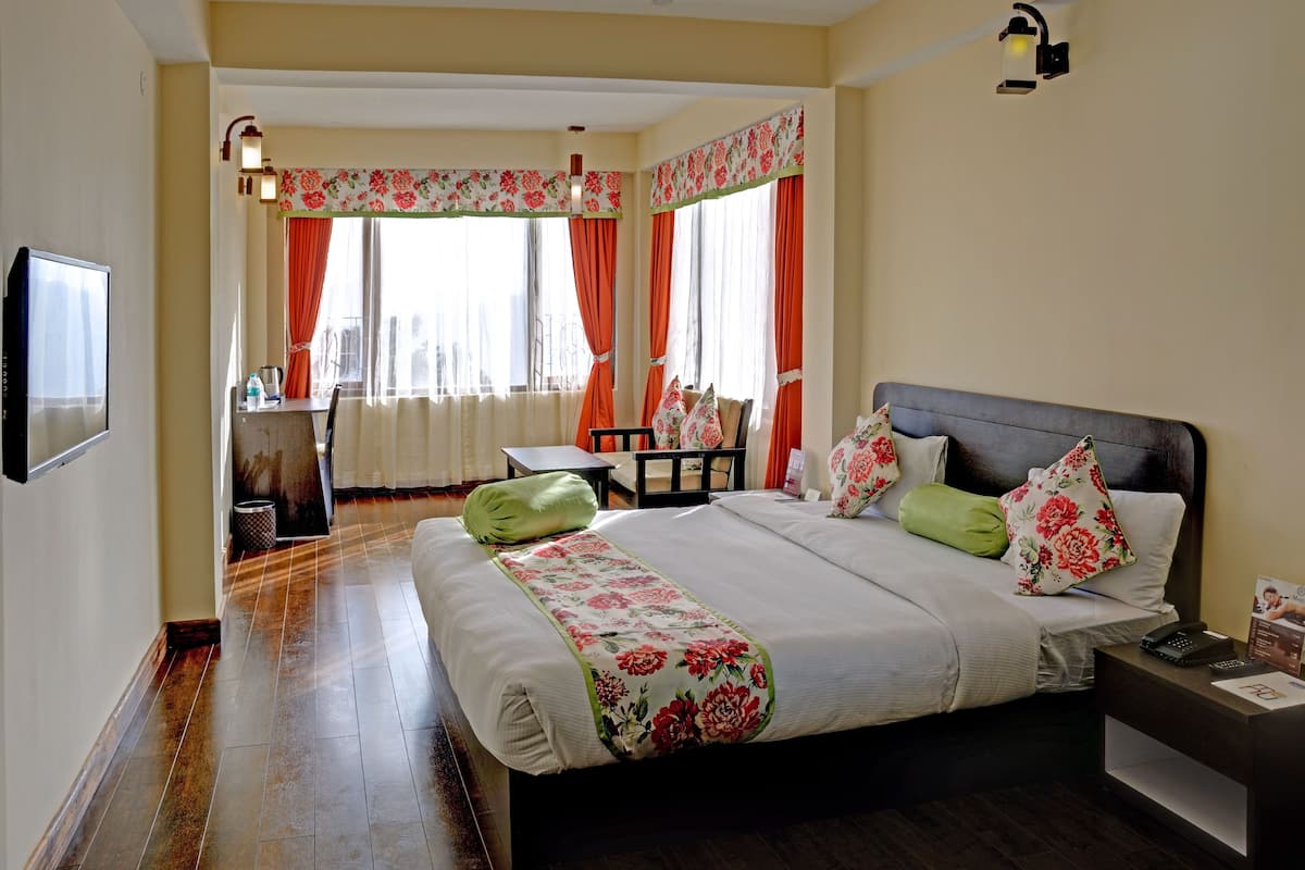 A hotel room with a large bed, a desk, and a chair. There is a window with curtains and a view of the city.