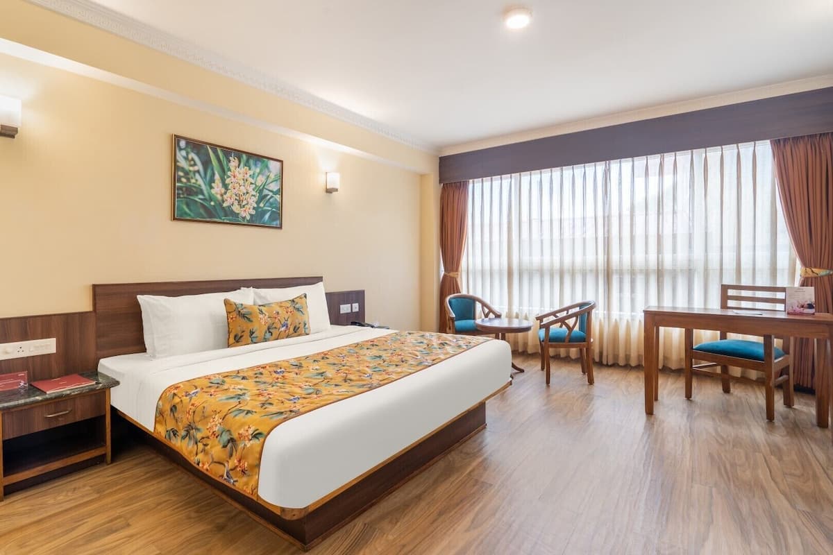 A hotel room with a large bed, a desk, two chairs, and a window with curtains.