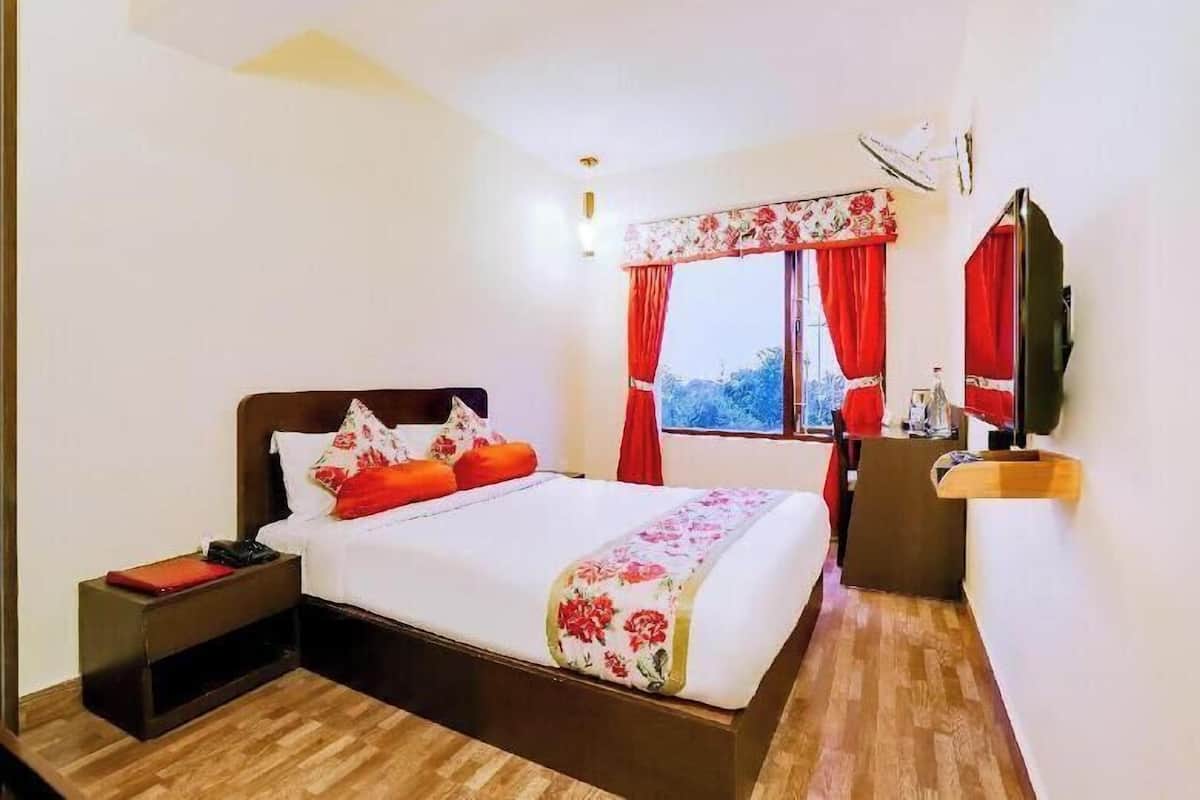 A hotel room with a bed, a nightstand, a TV, and a window with curtains.