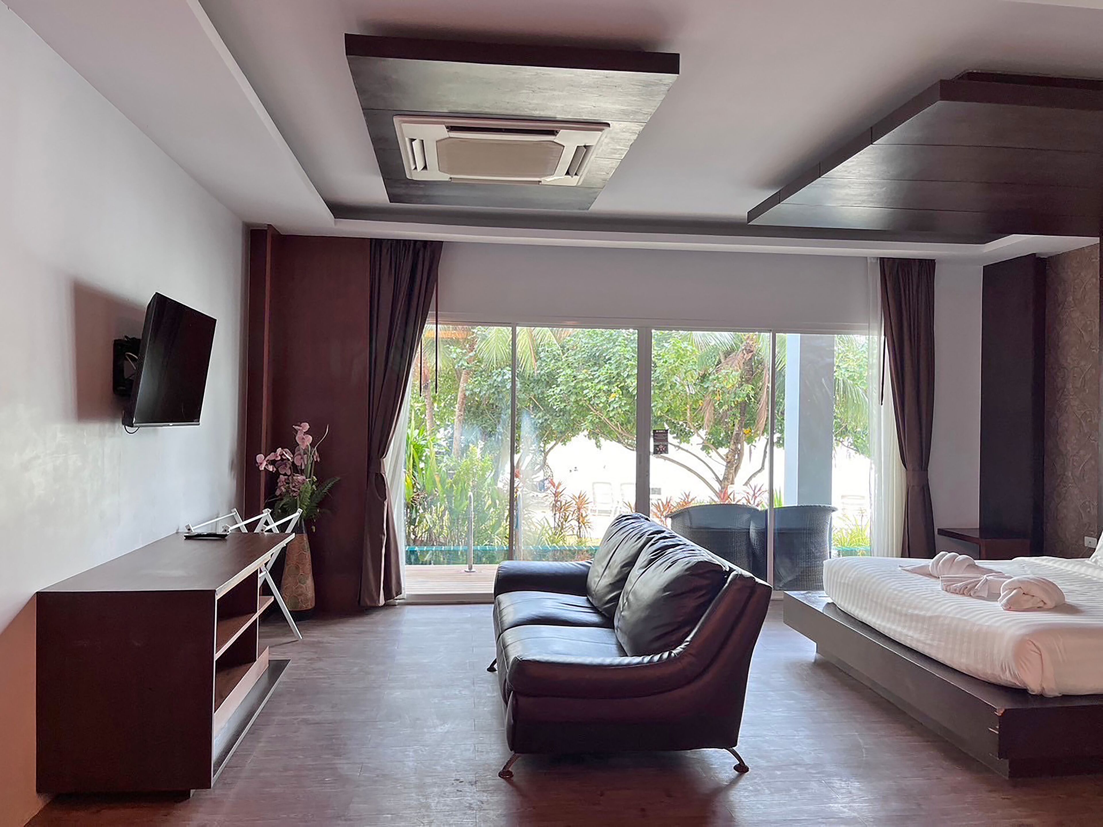 A modern hotel room with a sofa, a bed, a TV, and a large window with a view of greenery.