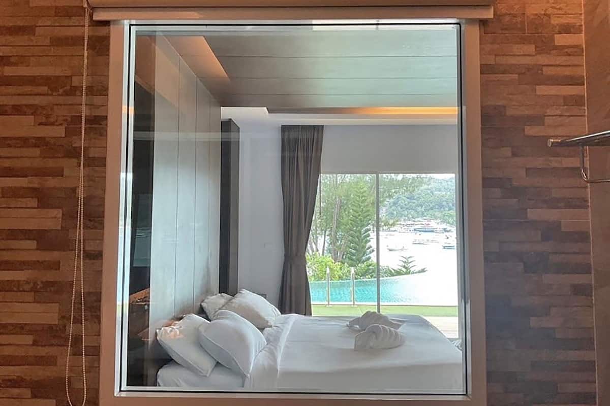Ein Hotelzimmer mit großem Fenster, einem Bett mit weißer Bettwäsche und Blick auf einen Pool und Grünflächen.