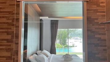 A hotel room with a large window, a bed with white linens, and a view of a pool and greenery.