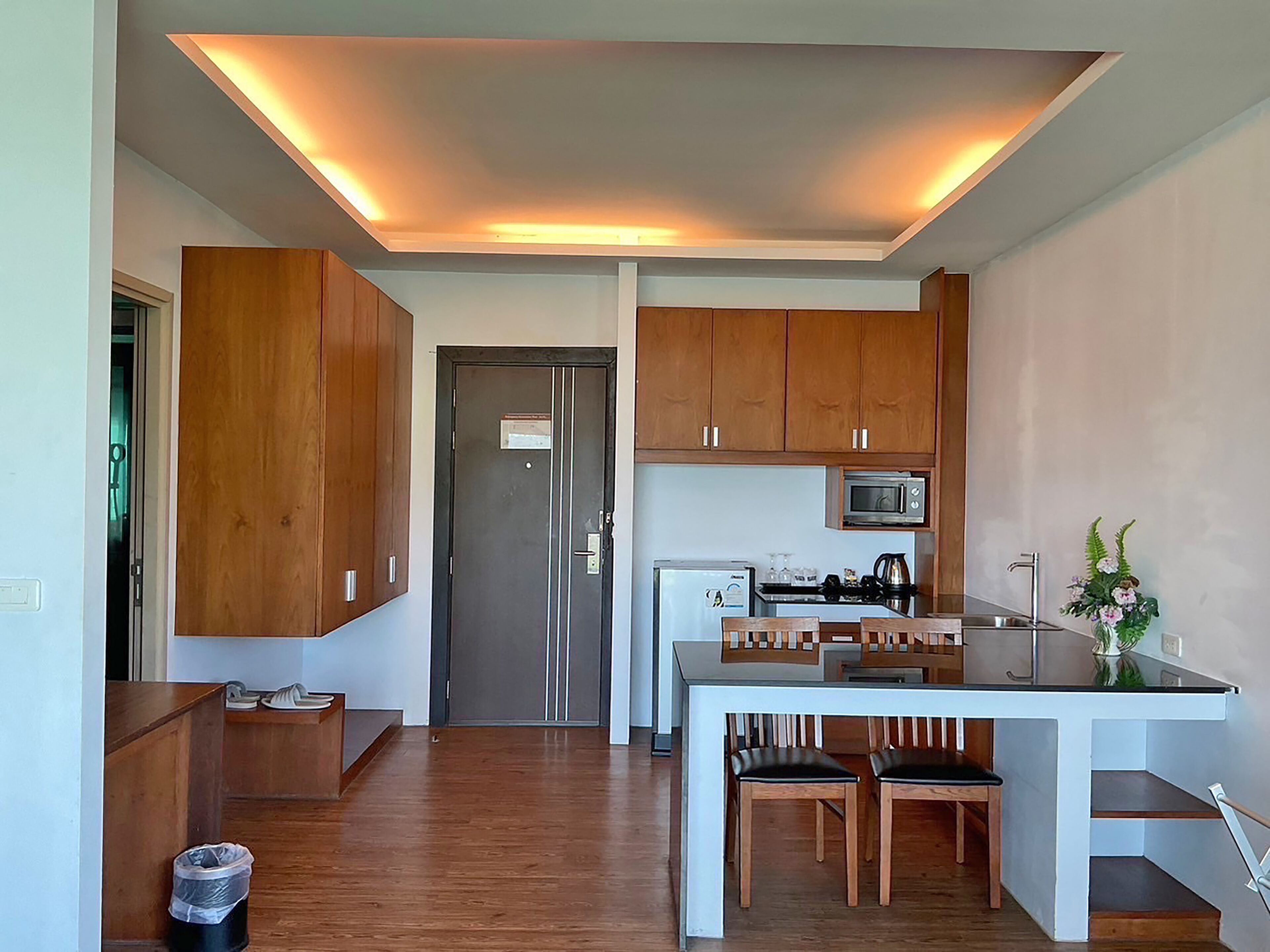 A compact kitchen with wooden cabinets, a microwave, a refrigerator, and a dining area with two chairs.