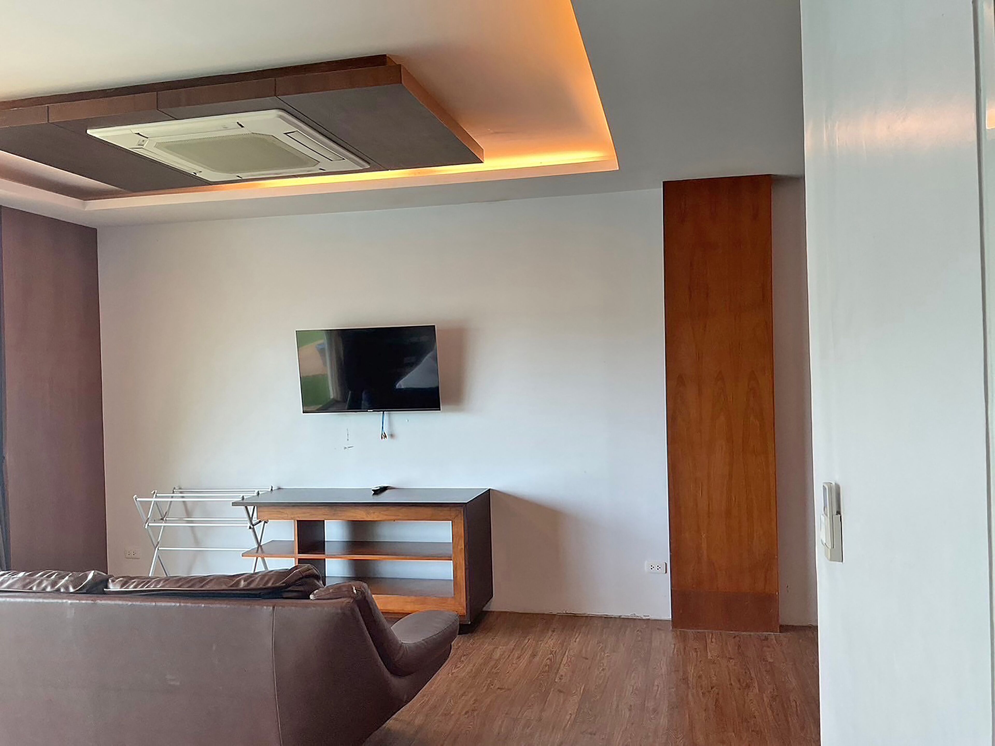 Ein modernes Wohnzimmer mit einem flachbildfernseher an der Wand, einem Holzschrank und einem Ledersofa.