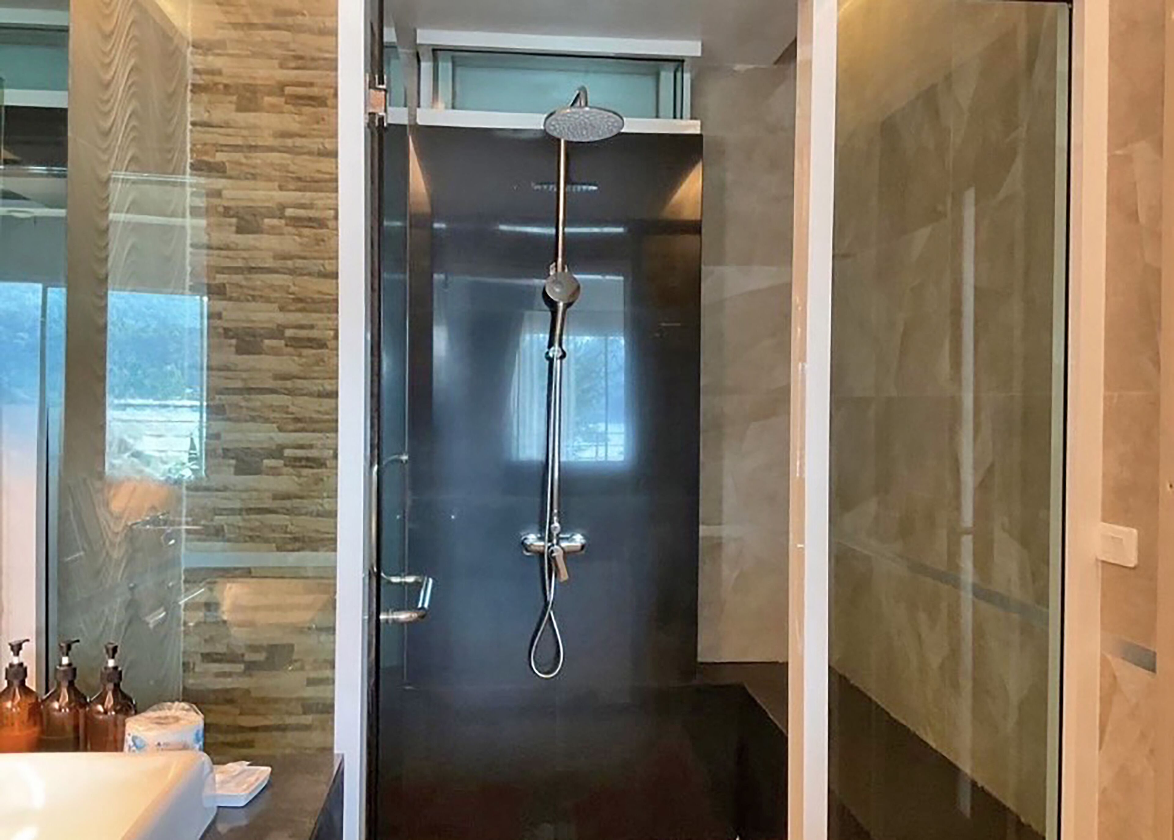 A modern bathroom with a glass-enclosed shower, a visible toilet paper dispenser, and a sink area.