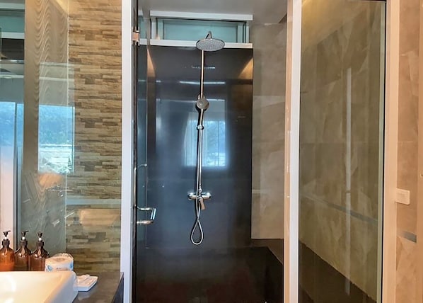 Un baño moderno con ducha de vidrio, dispensador de papel higiénico visible y zona de lavabo.