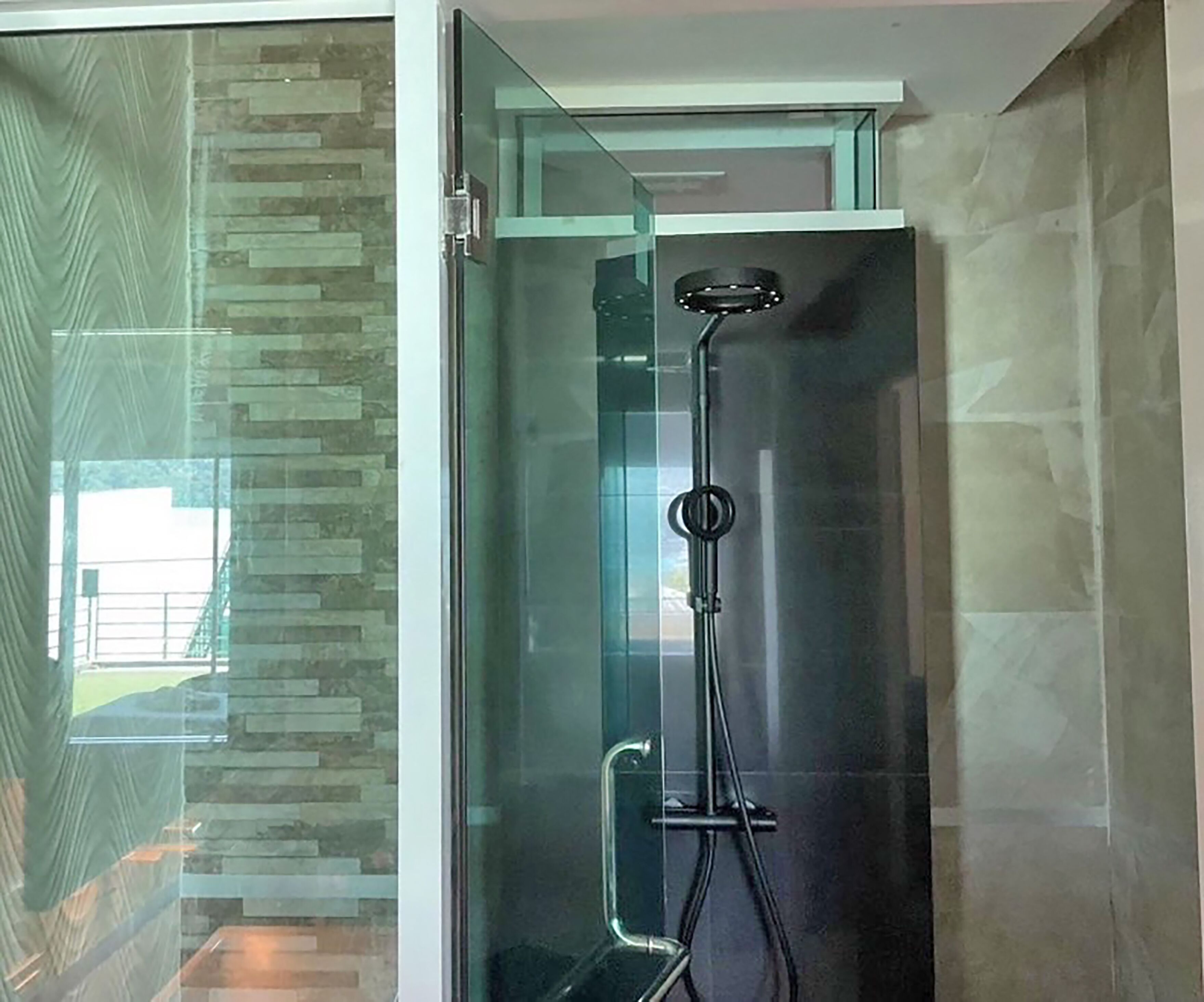 A modern shower with a glass enclosure, a handheld showerhead, and a wall-mounted control panel.