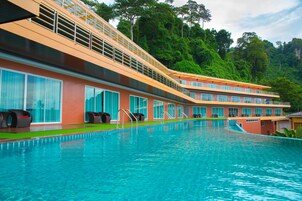 Et hotel med swimmingpool, flere balkoner og frodig, grøn skov i baggrunden.