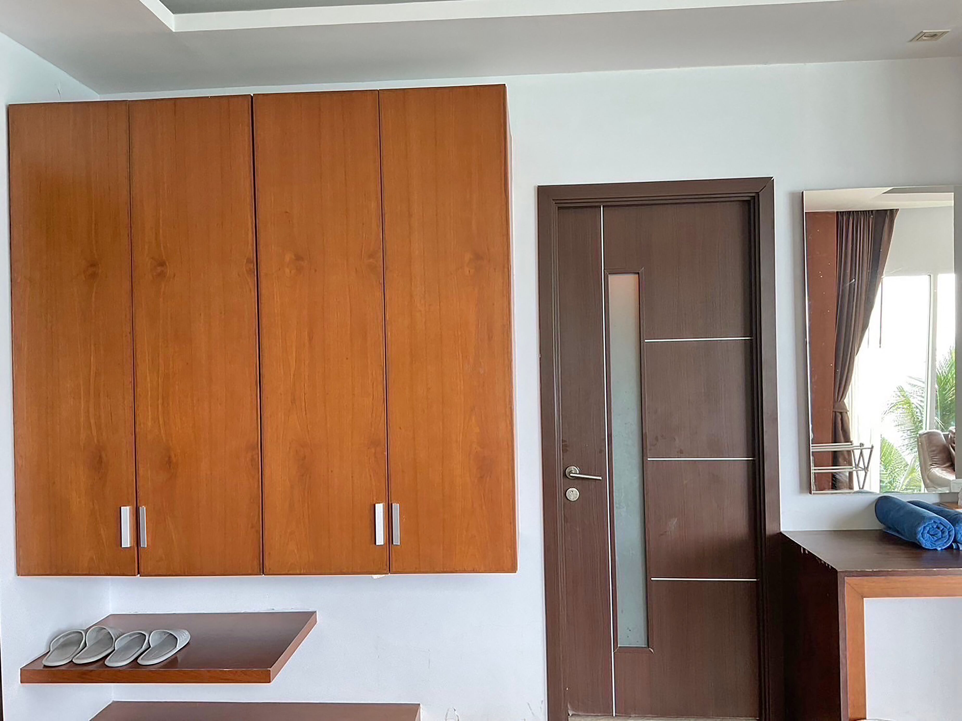 A room with a large wooden wardrobe, a door with a glass panel, and a small table with a towel.