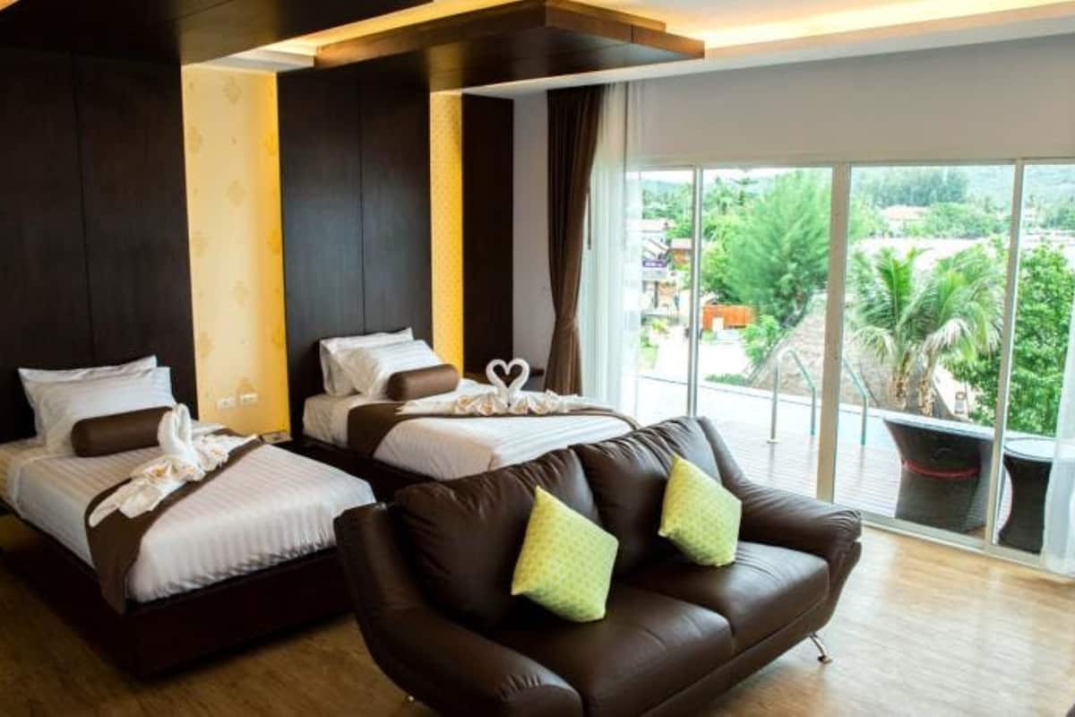 Ein Hotelzimmer mit zwei Betten, einem braunen Ledersofa und einem großen Fenster mit Blick auf Grünflächen.