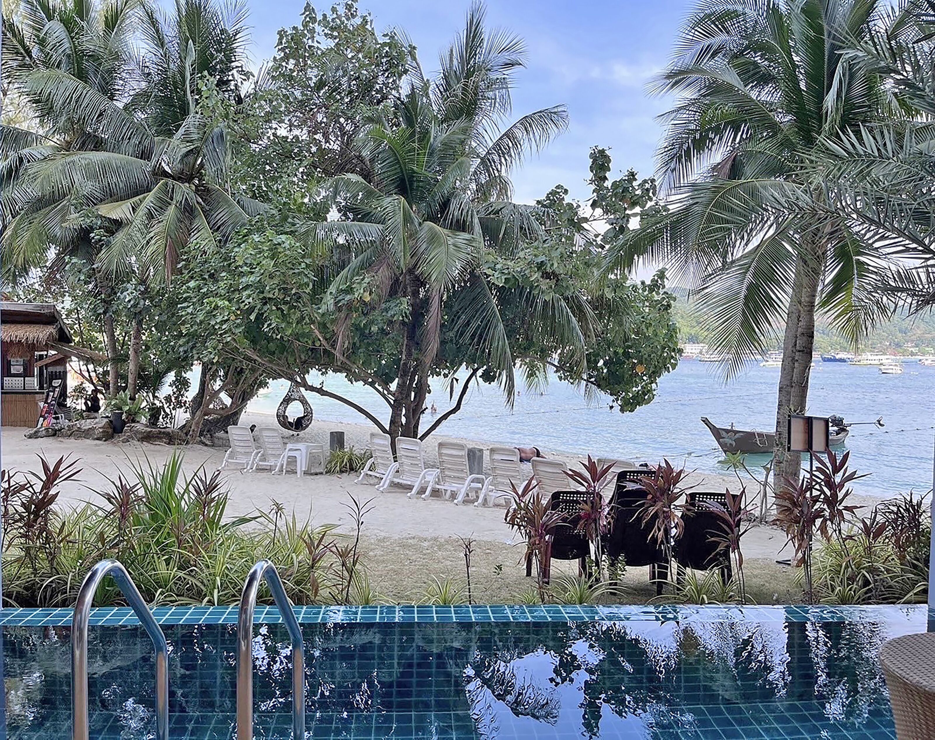 A poolside area with lounge chairs, a small building, and a view of the sea.