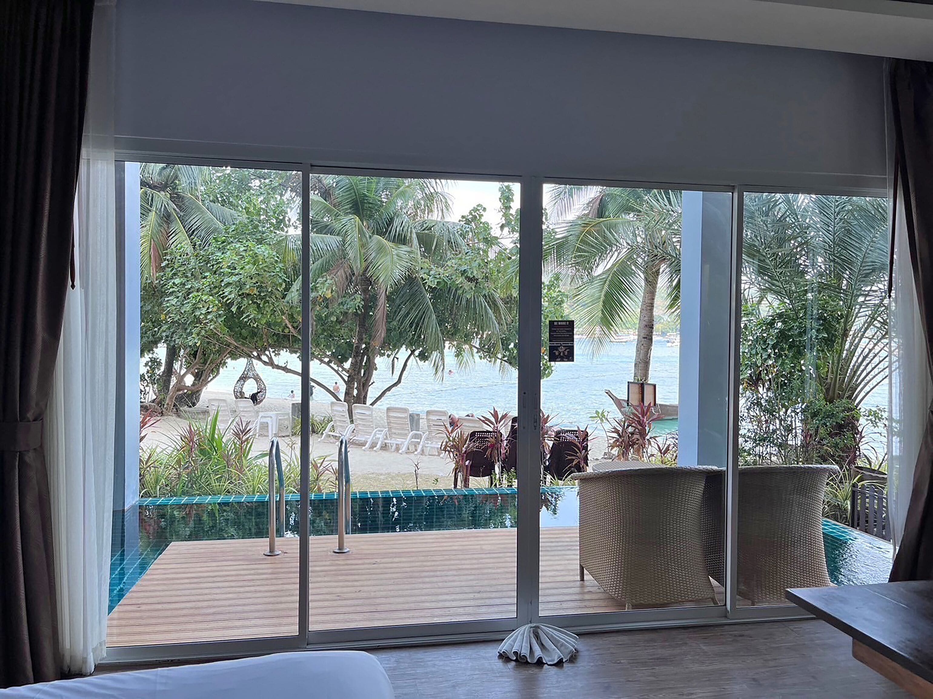 Una habitación con un amplio ventanal corredera que da a una zona de piscina con sillones reclinables y vista al mar.