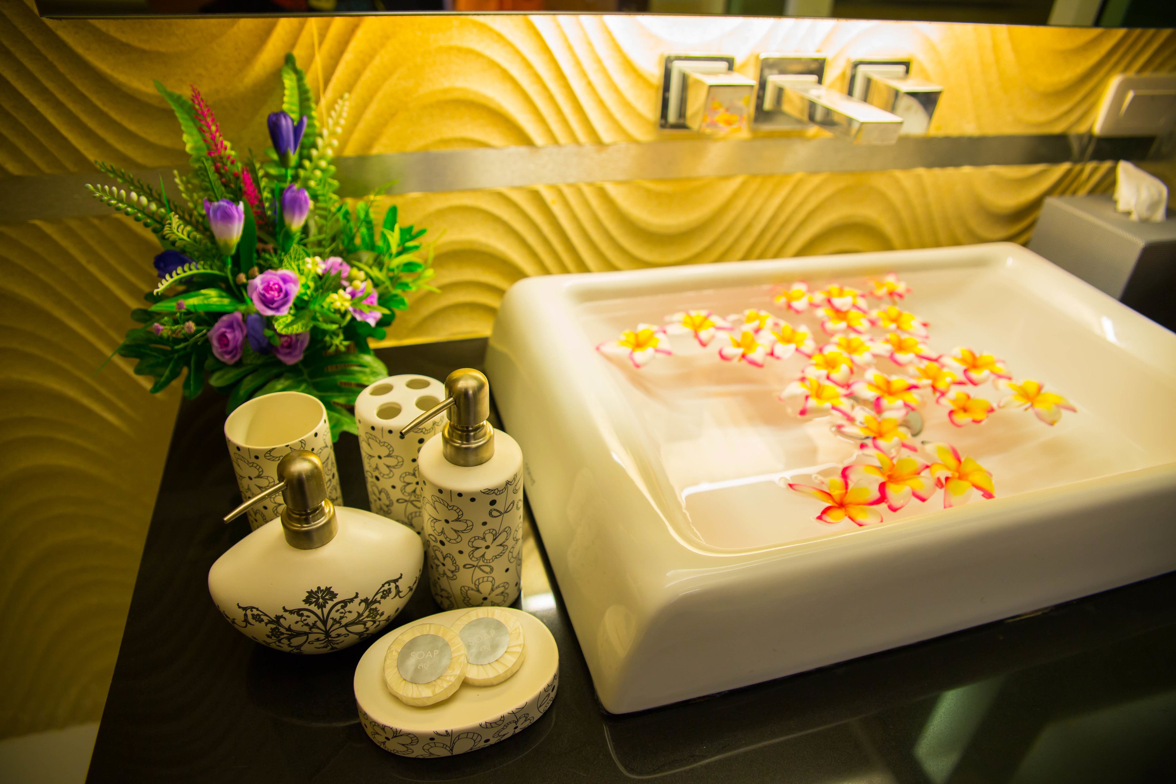 A bathroom with a white sink, floral decorations, and toiletries on a black countertop.