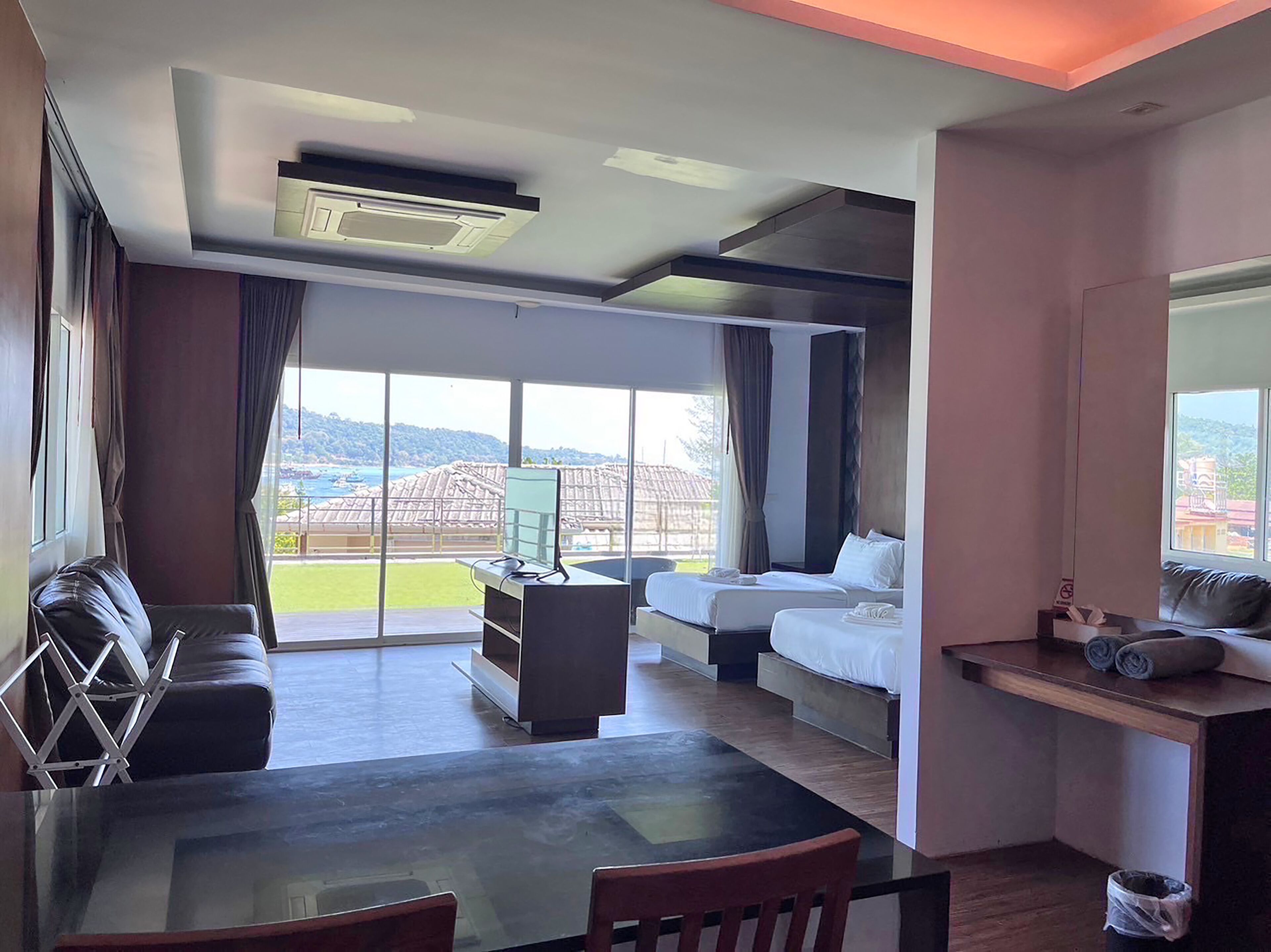 A hotel room with a balcony, a dining table, a sofa, a bed, and a TV.