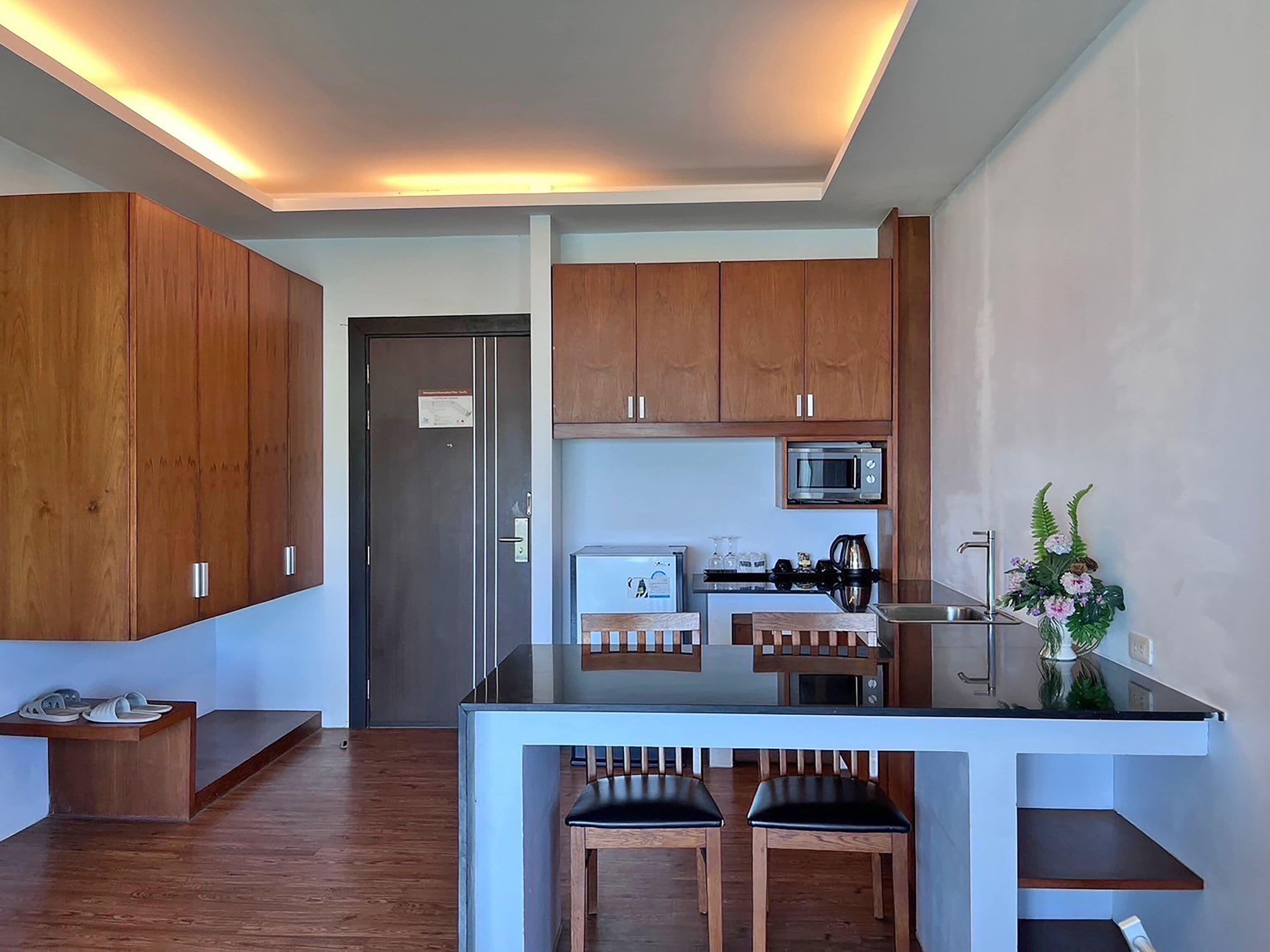 A modern kitchen with wooden cabinets, a microwave, a coffee maker, and a small dining area with two chairs.