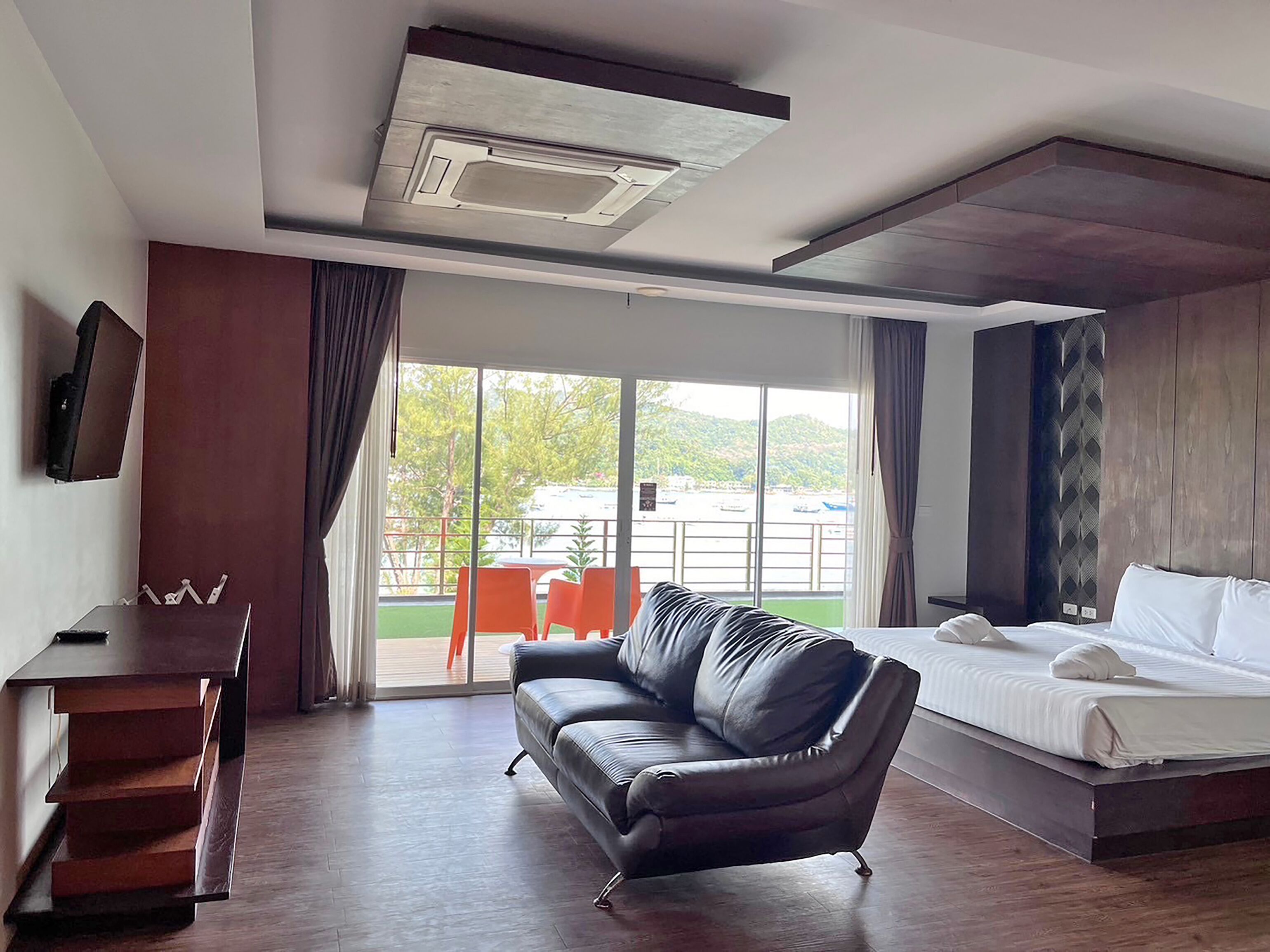 Una habitación de hotel moderna con una cama, un sofá de cuero, un escritorio y un ventanal que ofrece vistas al exterior.