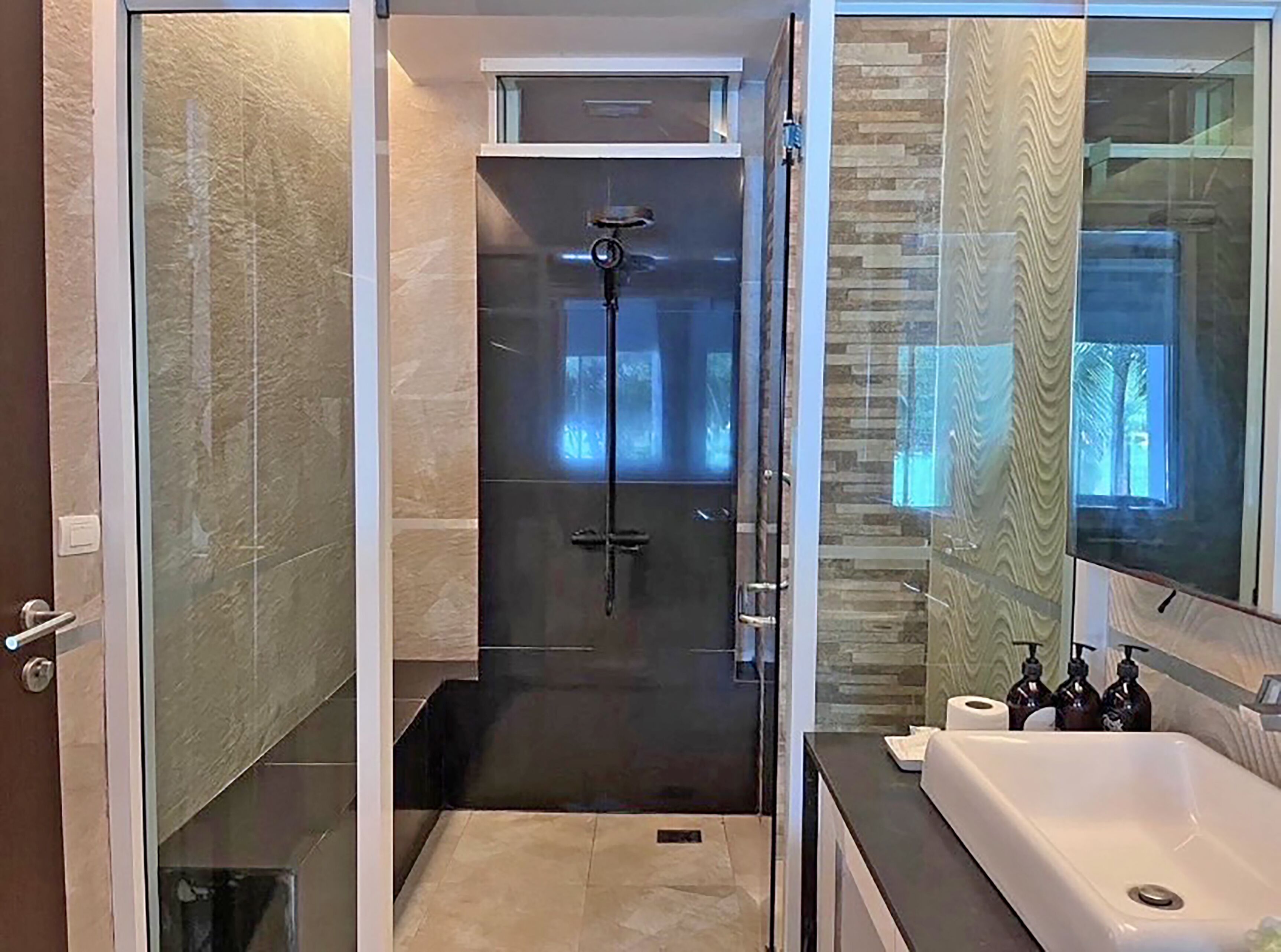 A modern bathroom with a glass-enclosed shower, a white bathtub, and a vanity with toiletries.