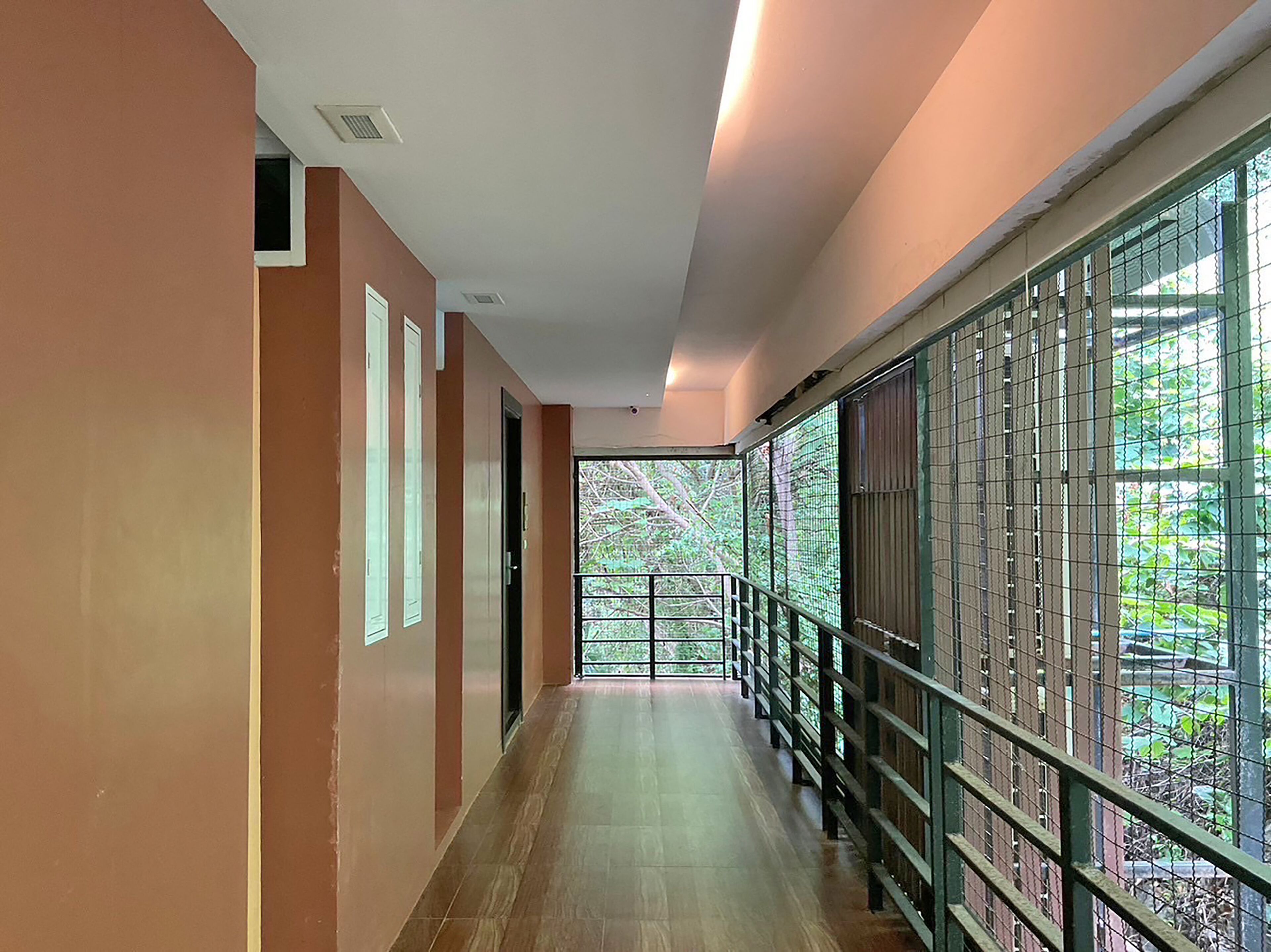 Un couloir doté d’un plancher en bois, de murs de couleur beige et d’une rambarde en métal, d’où l’on peut admirer la verdure à l’extérieur.
