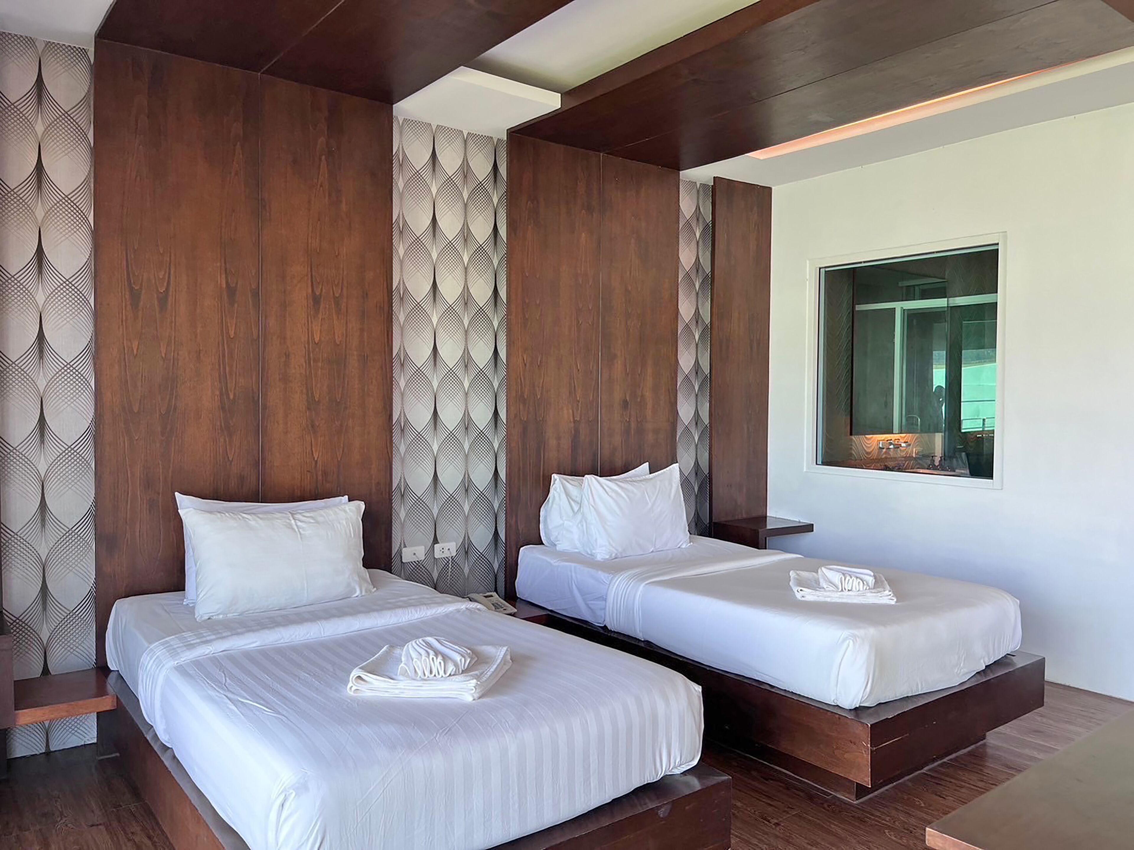 A hotel room with two beds, wooden paneling, a large mirror, and a window.