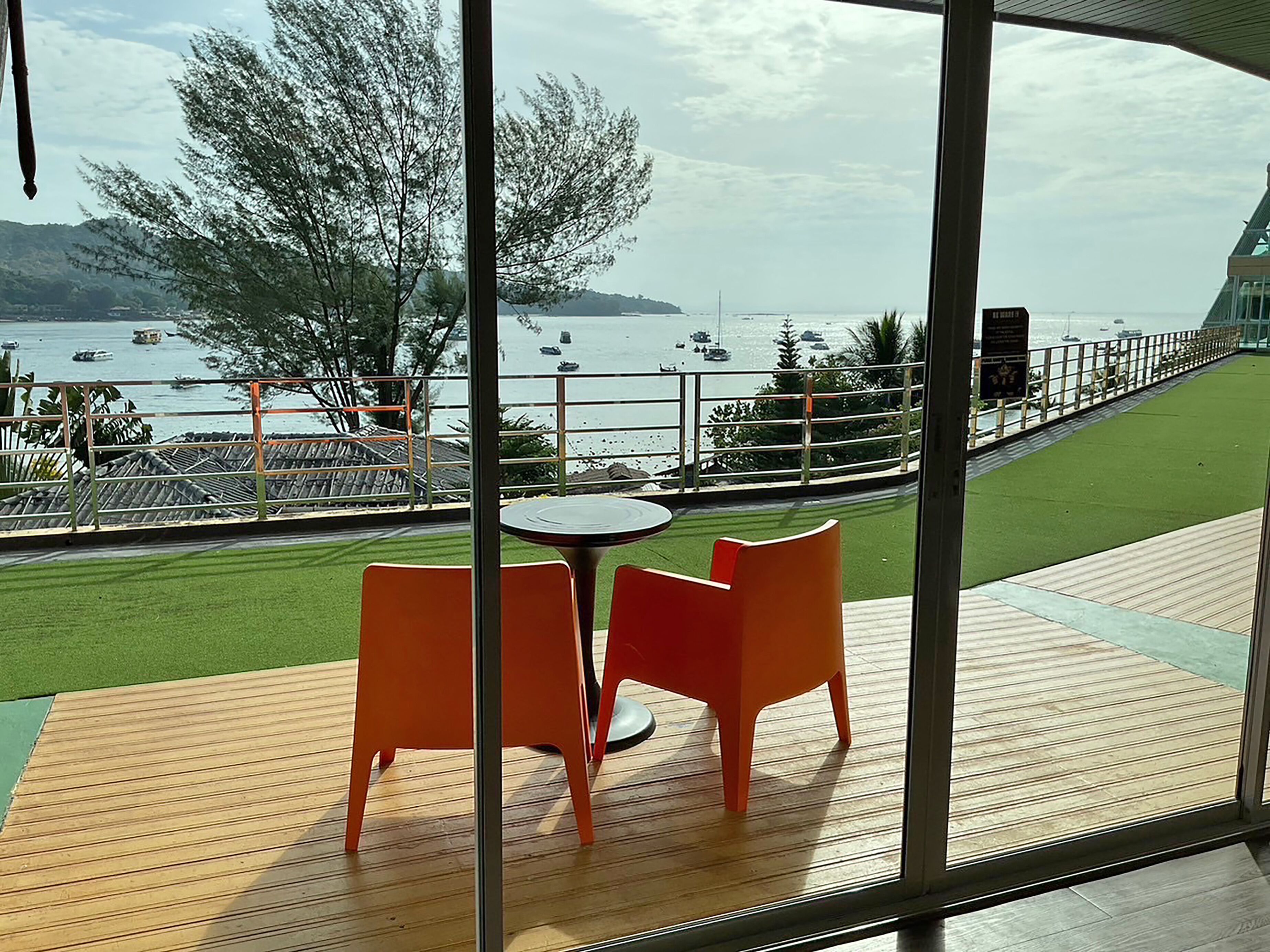 A balcony with a table and chairs, overlooking a body of water with boats and a distant shoreline.