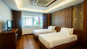 A hotel room with two beds, a wooden desk, a television, and a window with curtains.
