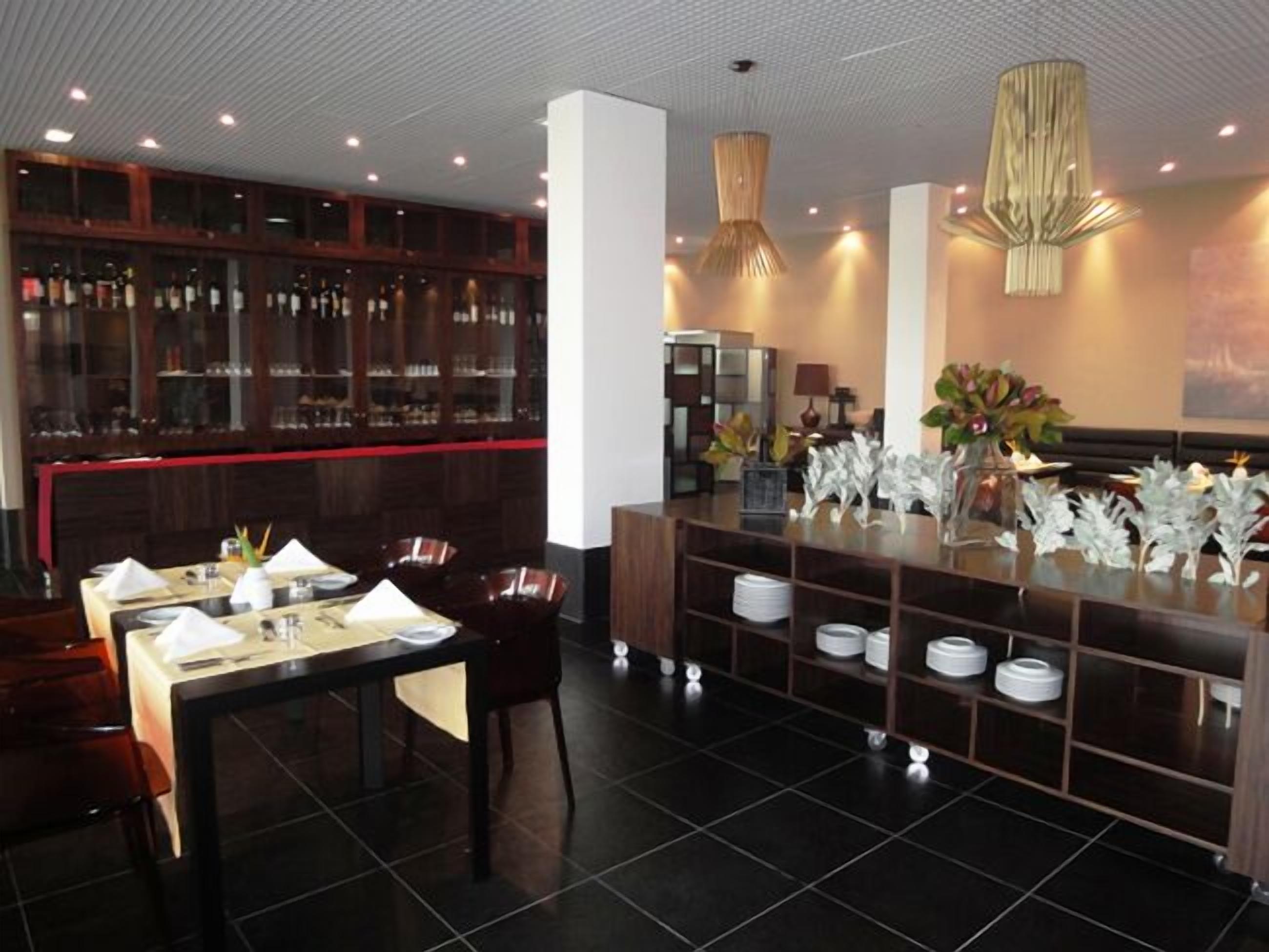 A restaurant with a bar area, dark wooden furniture, and modern lighting fixtures.