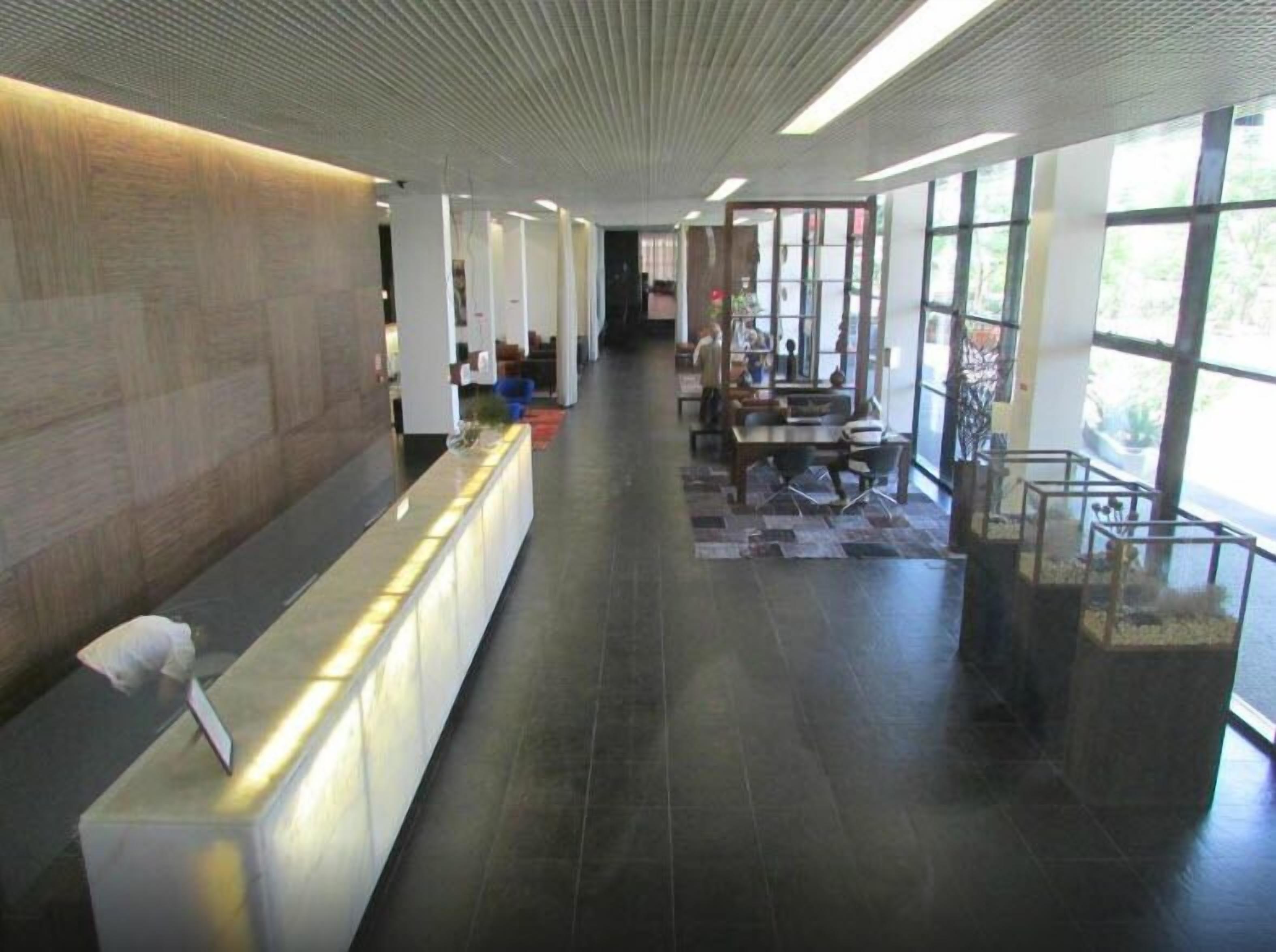 A modern reception area with a long reception desk, a seating area with tables and chairs, and large windows allowing natural light.