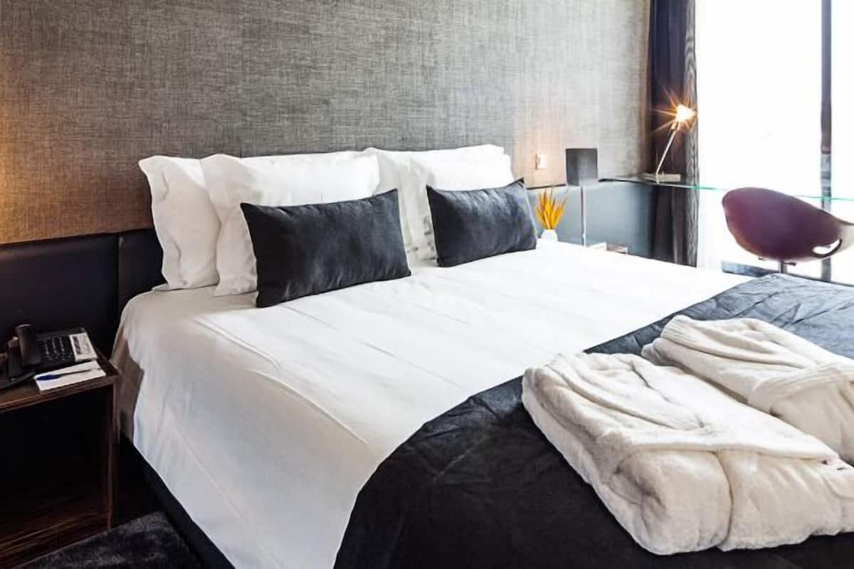A hotel room with a large bed, a bedside table with a lamp, a chair, and a view of the outdoors.