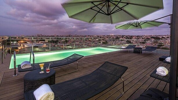 A rooftop pool area with lounge chairs and umbrellas, overlooking a cityscape.