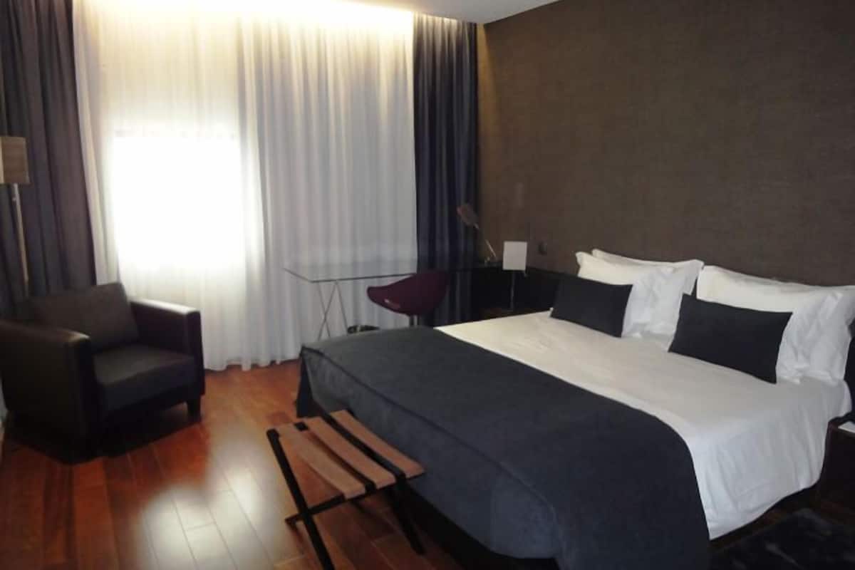 A modern hotel room with a large bed, a desk, and a chair.