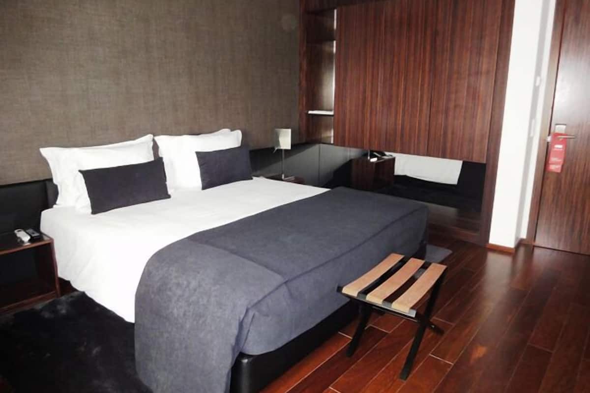 A modern hotel room with a large bed, wooden flooring, and a built-in wardrobe.