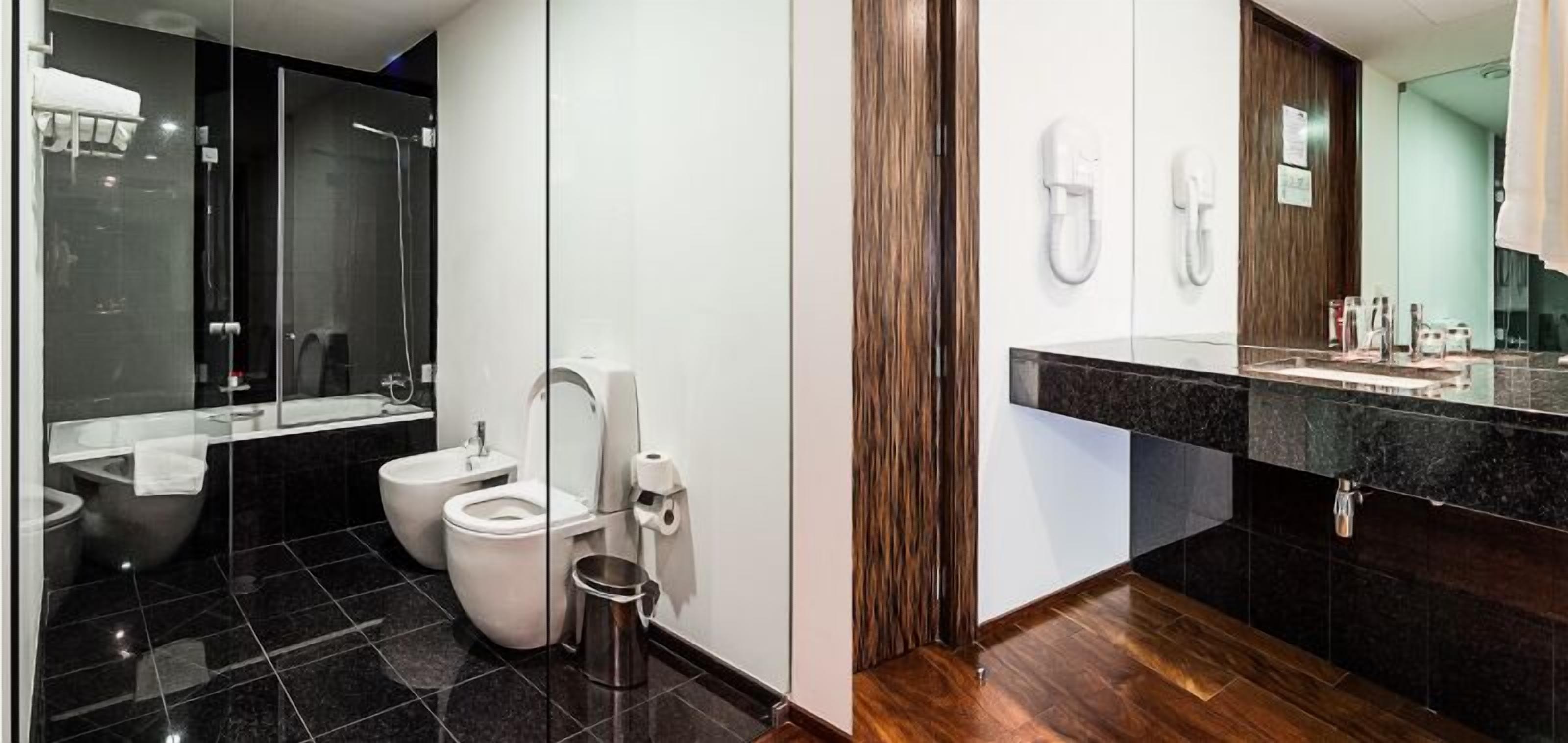 A modern bathroom with a glass shower enclosure, a toilet, a bidet, and a vanity with a mirror.