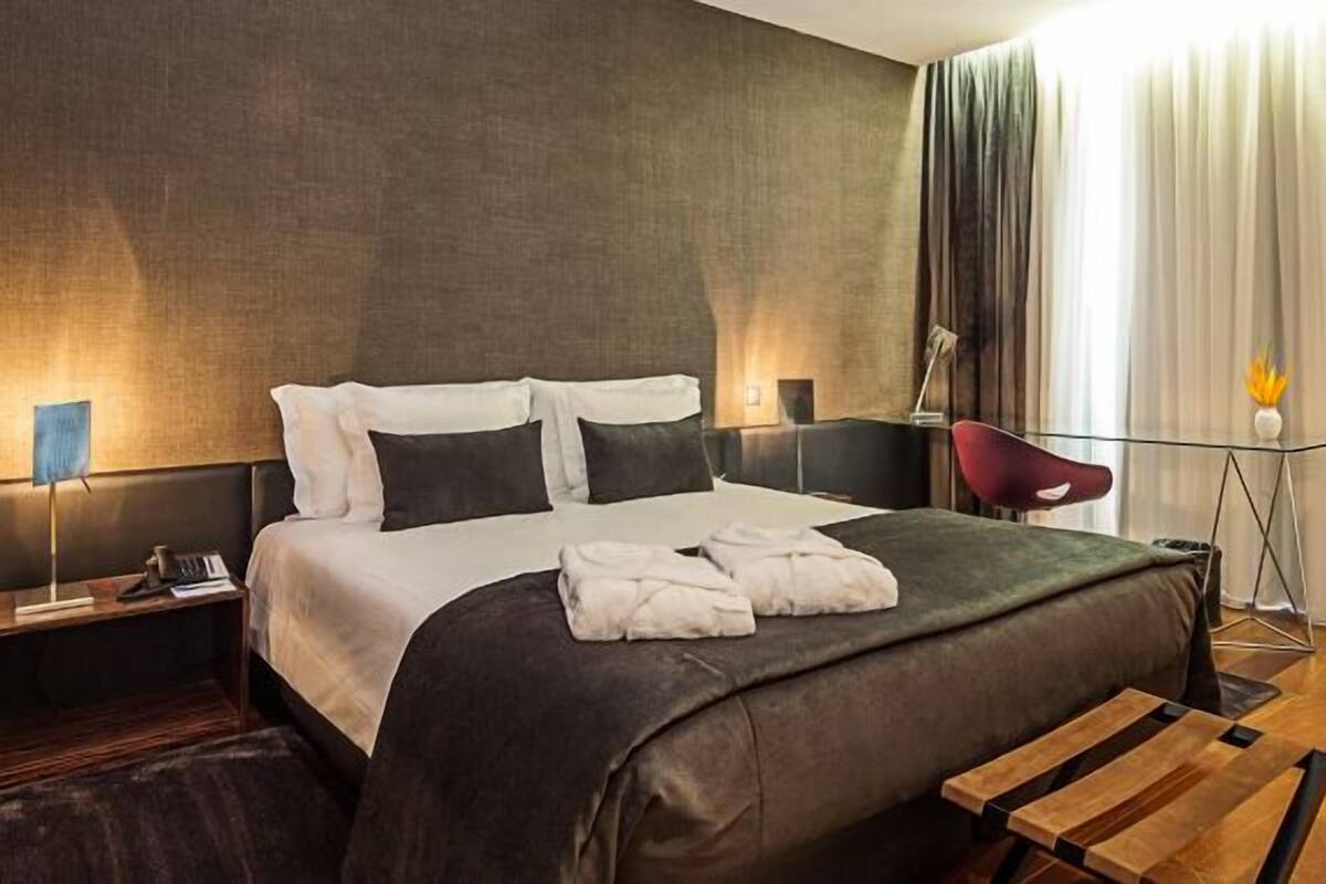 A modern hotel room with a large bed, a desk, a chair, and a sofa.